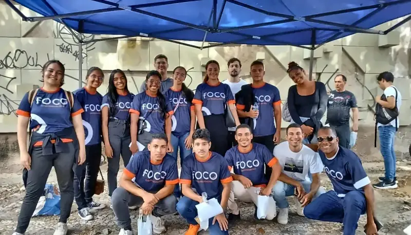 Alunos do Foco com a camisa azul do curso, reunidos ao ar livre debaixo de uma tenda azul