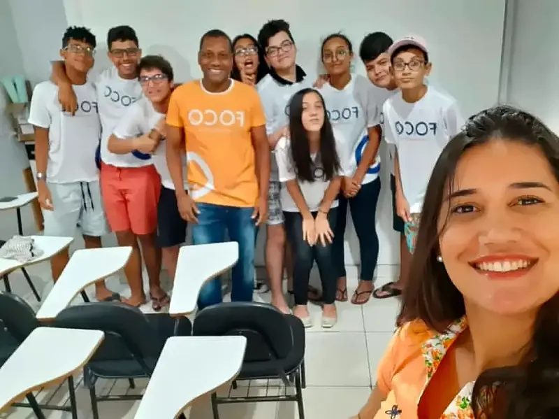 Professora faz selfie com a turma do Foco, de camisa branca do curso, ao fundo