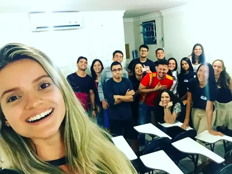 Professora sorridente faz selfie com a turma em pé ao fundo da sala